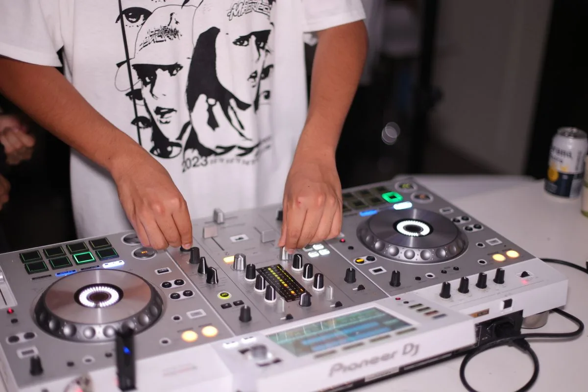 Manos de un DJ operando una consola de mezcla. Imagen de referencia para una marca ficticia.