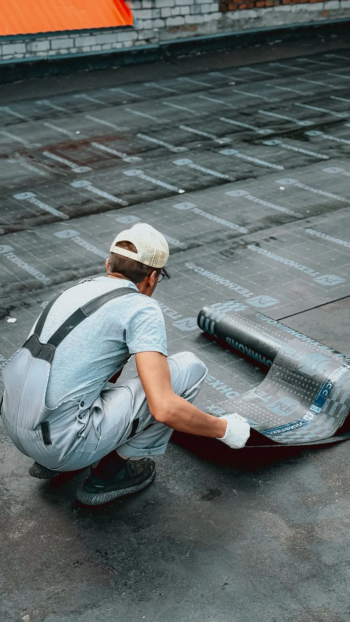 Trabajador colocando una membrana impermeabilizante en una azotea. Imagen de referencia para una marca ficticia.