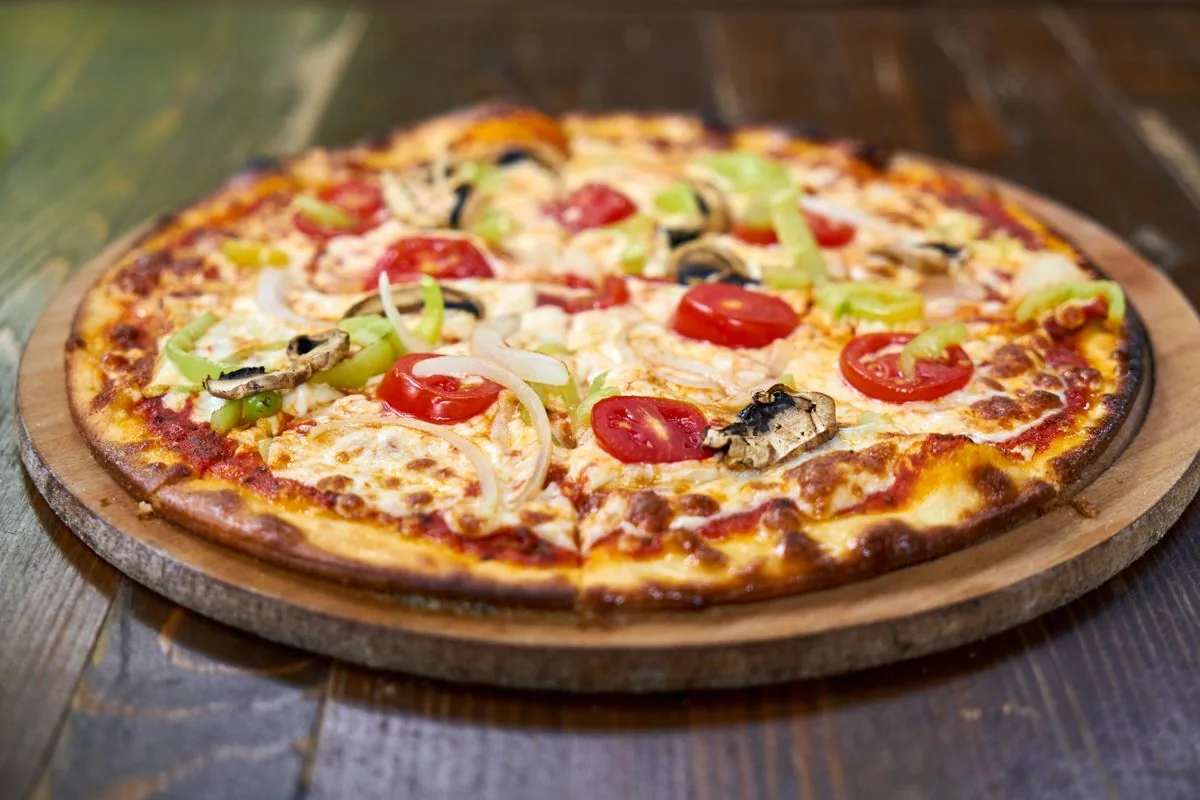 Pizza con vegetales y queso sobre una tabla. Imagen de referencia para una marca ficticia.